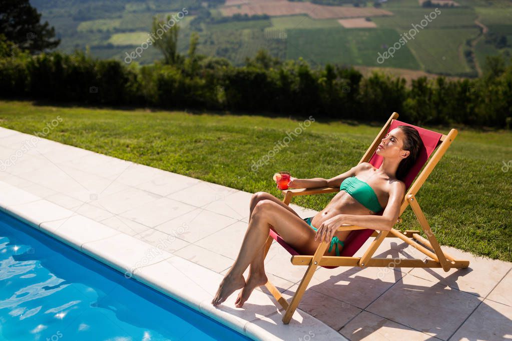 Glamorous woman enjoying her drink poolside and tanning