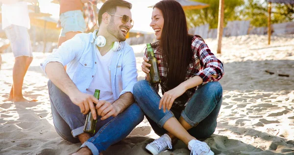 幸せな若いカップルはビールを飲んで 日没の間にビーチで楽しんでいます — ストック写真