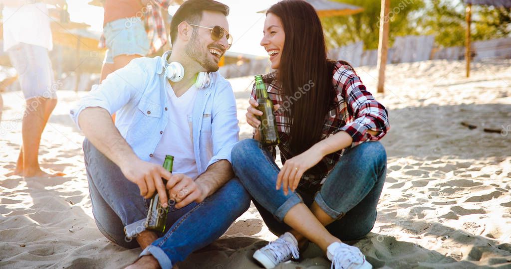 Happy young couple drinking beer and having fun at the beach during sunset