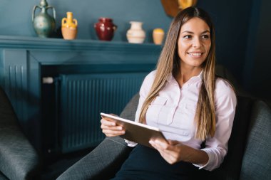 Tablet tutan genç güzel gülümseyen uzun saçlı esmer kadın portresi