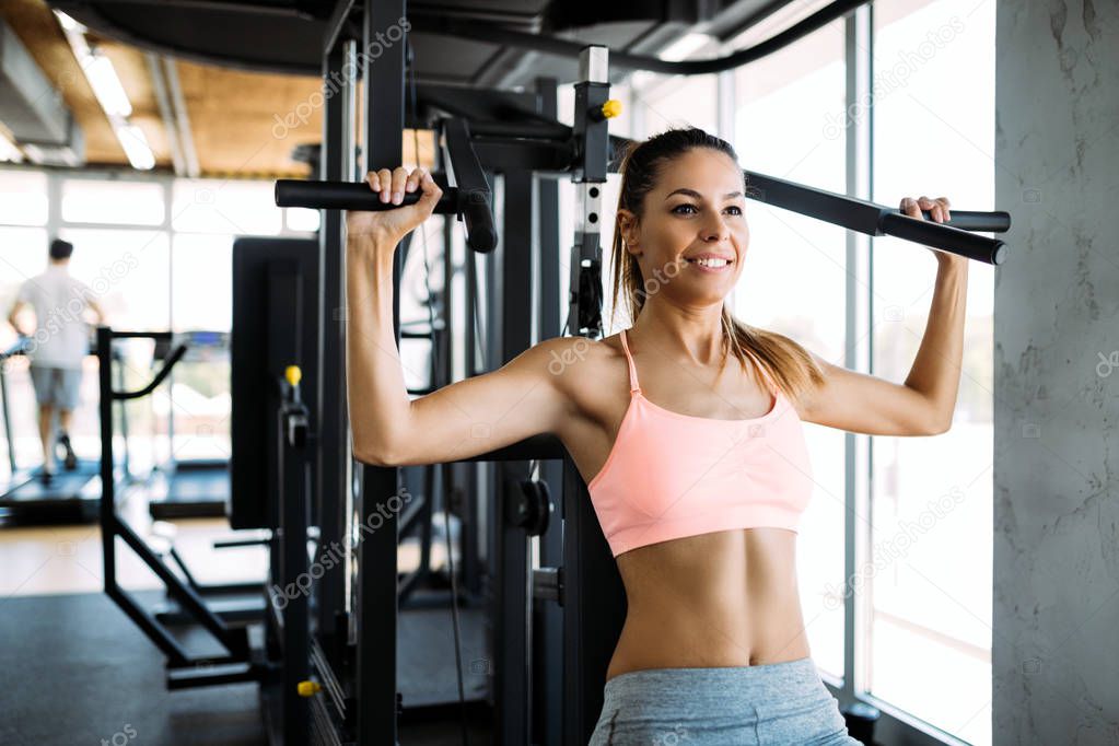 Happy young woman exercising on a shoulder press in fitness center