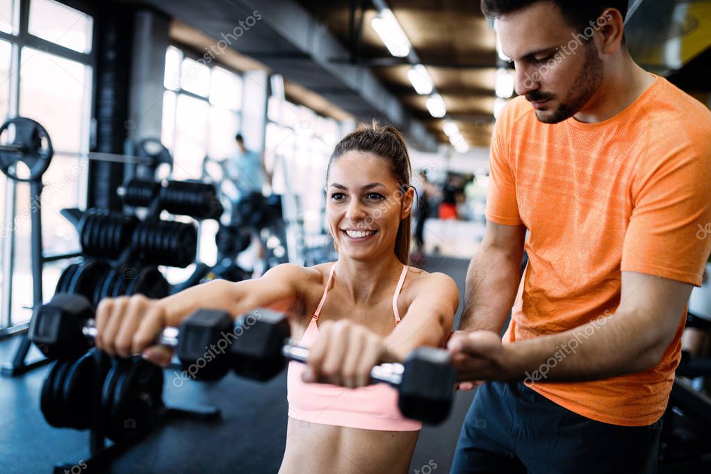 Beautiful woman helped by trainer in gym