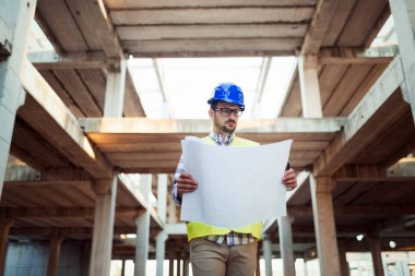Erkek sitesi yüklenici mühendis baret inşaat alanında mavi baskı kağıdı tutan ile portresi,