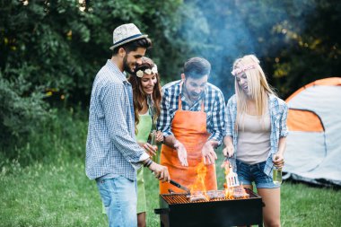 Neşeli arkadaşlar doğada vakit geçirip barbekü yapıyorlar.