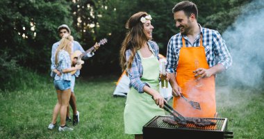 Mutlu insanlar kamp yapıyor ve dışarıda bbq partisi veriyor.