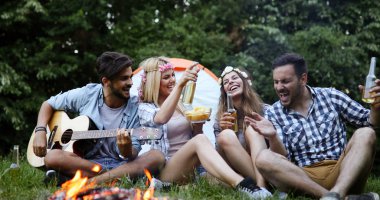 Mutlu arkadaşlar müzik çalıyor ve doğada şenlik ateşinin keyfini çıkarıyorlar.