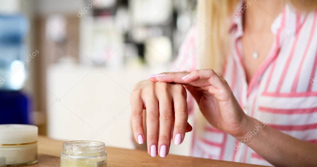 Beautiful woman applying moisturizing cream on hands