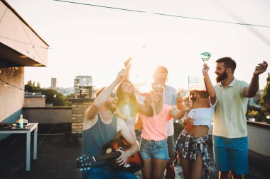 Bir grup mutlu genç arkadaş çatıda parti veriyor.