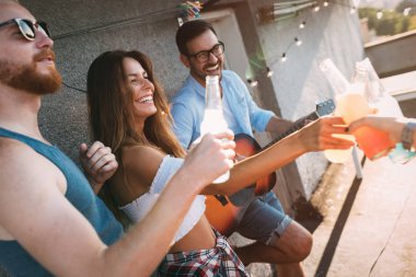 Bir grup mutlu genç arkadaş çatıda parti veriyor.