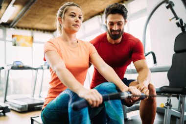 Genç ve güzel bir kadın spor salonunda antrenörle egzersiz yapıyor.