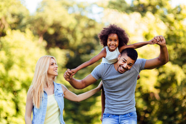 Портрет молодого отца, несущего дочь на спине в природе
