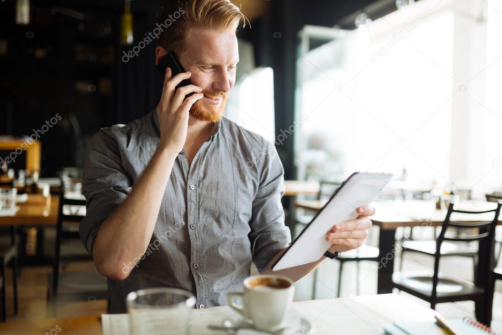 Busy handsome smart blogger multitasking in cafe