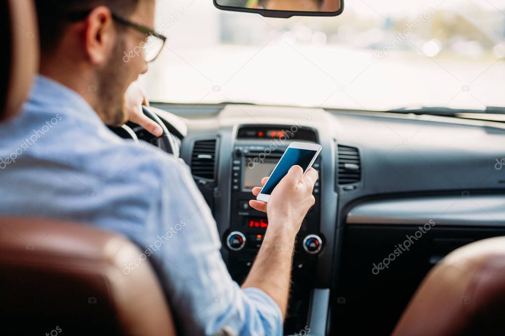 Handsome businessman ignoring safety and texting onmobile phone while driving