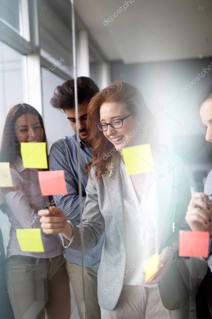 Creative business team looking at sticky notes on window in modern office