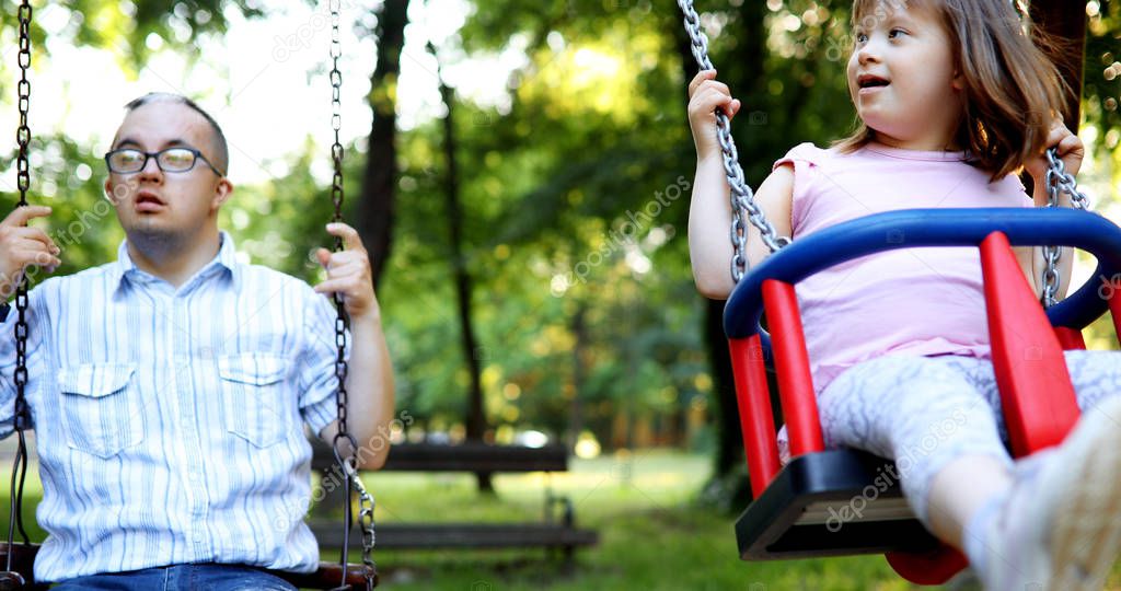 Portrait of man and girl with down syndrome swinging in park