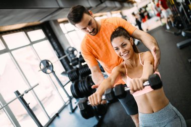 Genç ve güzel bir kadın spor salonunda antrenörle egzersiz yapıyor.