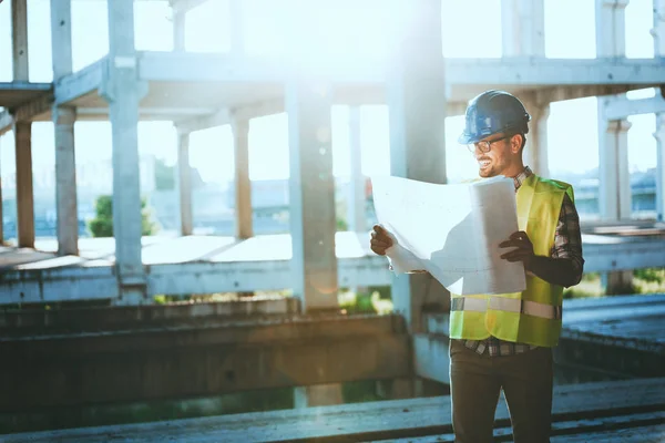 Portrait of male site contractor engineer with hard hat holding blue print paper at construction site,