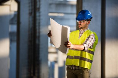 İnşaatta çalışan ve blueprint tutan yakışıklı mühendisi