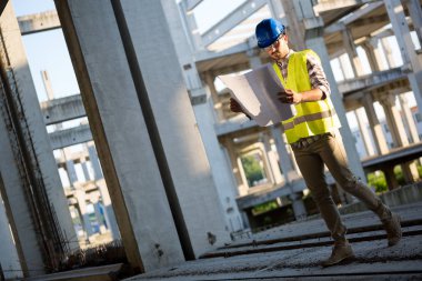 İnşaatta çalışan ve blueprint tutan yakışıklı mühendisi