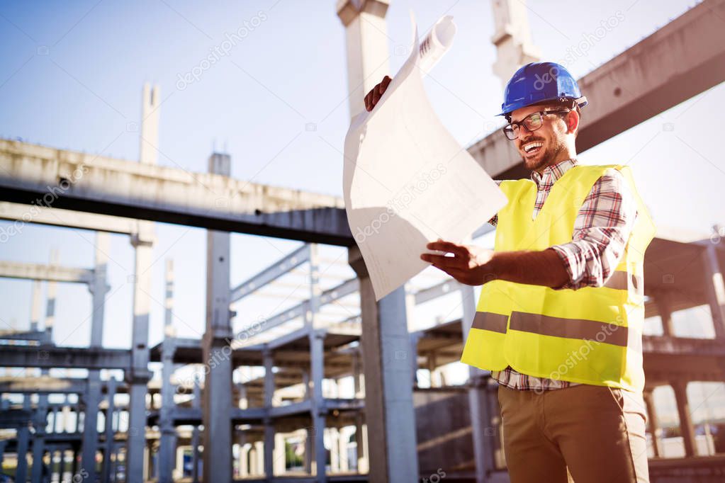 Handsome engineer working on construction site and holding blueprint