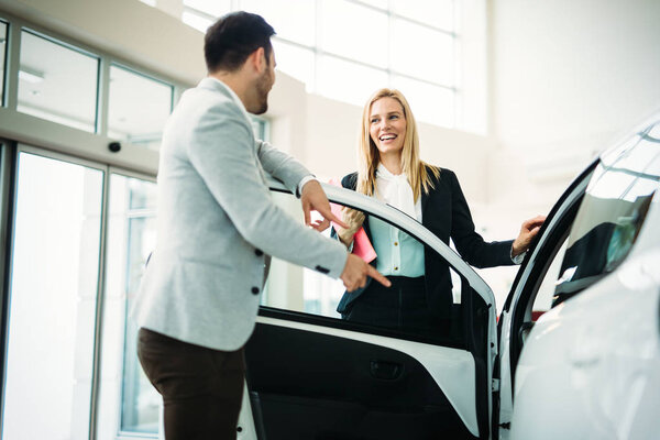 Дилер, показывающий новую модель автомобиля потенциальному покупателю в салоне