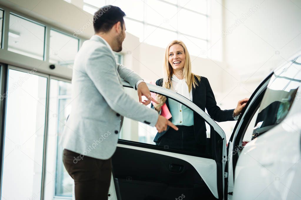 Dealer showing a new car model to the potential customer in saloon