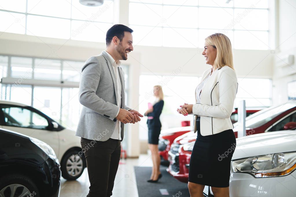 Woman is talking to handsome car dealership worker while choosing a car in dealership