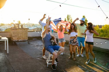 Bir grup mutlu genç arkadaş çatıda parti veriyor.