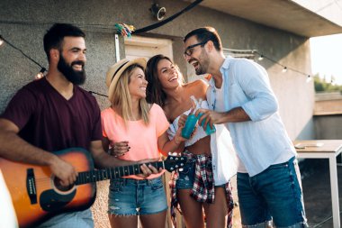 Bir grup mutlu genç arkadaş çatıda parti veriyor.
