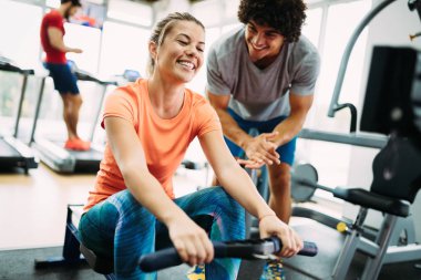 Genç ve güzel bir kadın spor salonunda antrenörle egzersiz yapıyor.