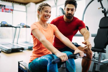 Genç ve güzel bir kadın spor salonunda antrenörle egzersiz yapıyor.