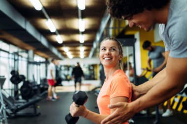 Genç ve güzel bir kadın spor salonunda antrenörle egzersiz yapıyor.