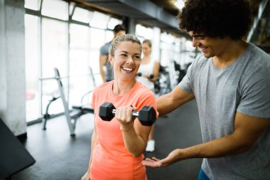 Genç ve güzel bir kadın spor salonunda antrenörle egzersiz yapıyor.
