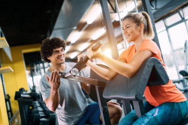 Genç ve güzel bir kadın spor salonunda antrenörle egzersiz yapıyor.