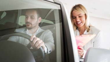 Satıcı salonda potansiyel müşteriye yeni bir araba modeli gösteriyor.