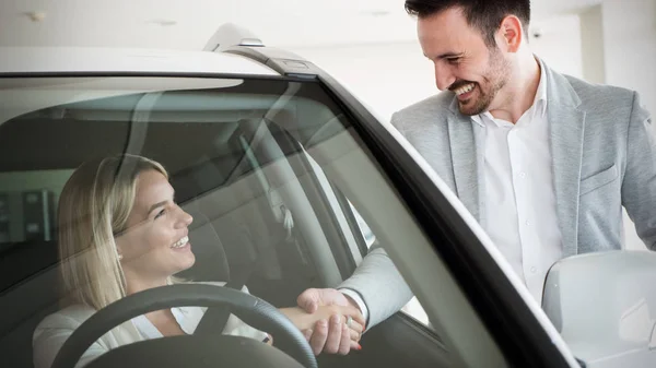 Woman buying a car in dealership sitting in her new auto, the salesman talking to her in the background