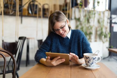 Mutlu genç kadın kahve içme ve tablet kahve dükkanında kullanma