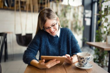 Mutlu genç kadın kahve içme ve tablet kahve dükkanında kullanma