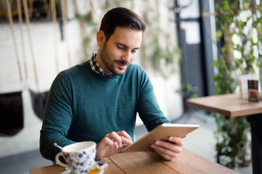 Yakışıklı genç gülümseyen ve tutan tablet bilgisayar kafede adam