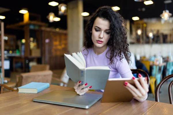 Junge Frau Liest Buch Und Hält Tablet Café — Stockfoto