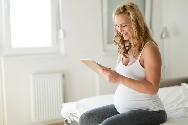 幸せな妊娠中の金髪女性の寝室でタブレットを使用して — ストック写真