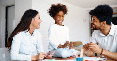 Anne ve baba evde çocuklarıyla birlikte resim çiziyorlar.