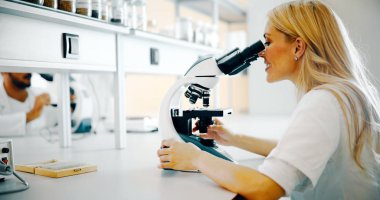 Laboratuvarda mikroskoptan bakan genç kadın bilim adamı.
