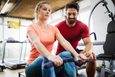 Genç ve güzel bir kadın spor salonunda antrenörle egzersiz yapıyor.