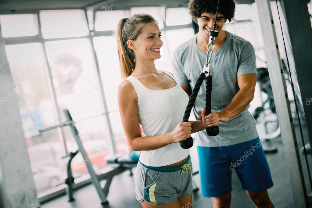 Young beautiful woman doing exercises with personal trainer in gym