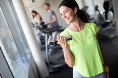 Genç ve güzel bir kadın spor salonunda halterle egzersiz yapıyor. Gülümseyen kızın eğitim sürecinden zevk almasına sevindim.