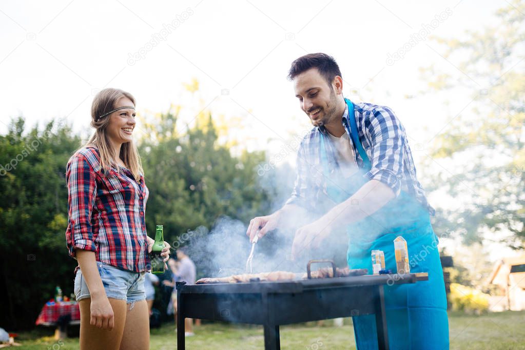 Happy friends grilling meat and enjoying barbecue party outdoors