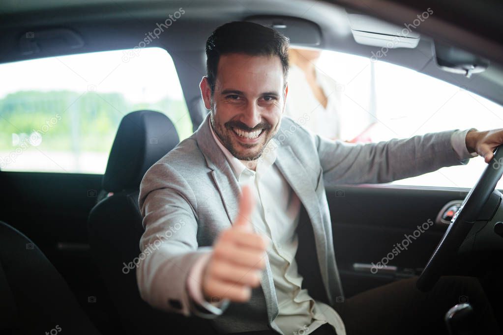 Portrait of handsome young man taking a car for test drive, sitting inside and smiling