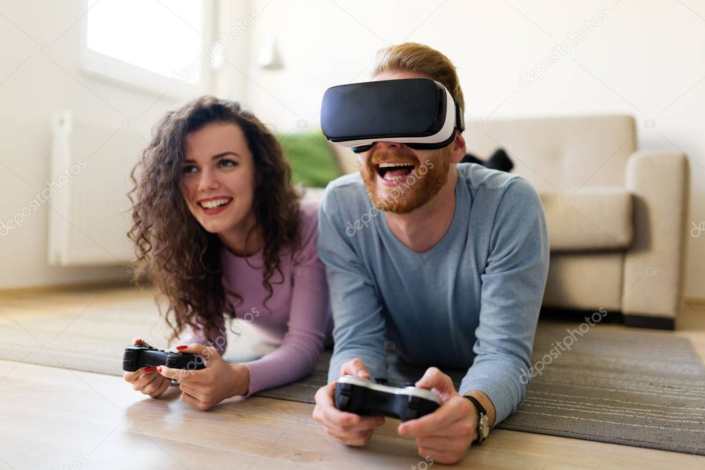 Happy young couple playing video games with virtual reality headsets at home