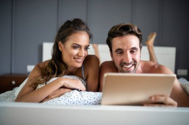 Mutlu çift tablet gibi görünüyor ve yatakta yatarken gülüyorlar.